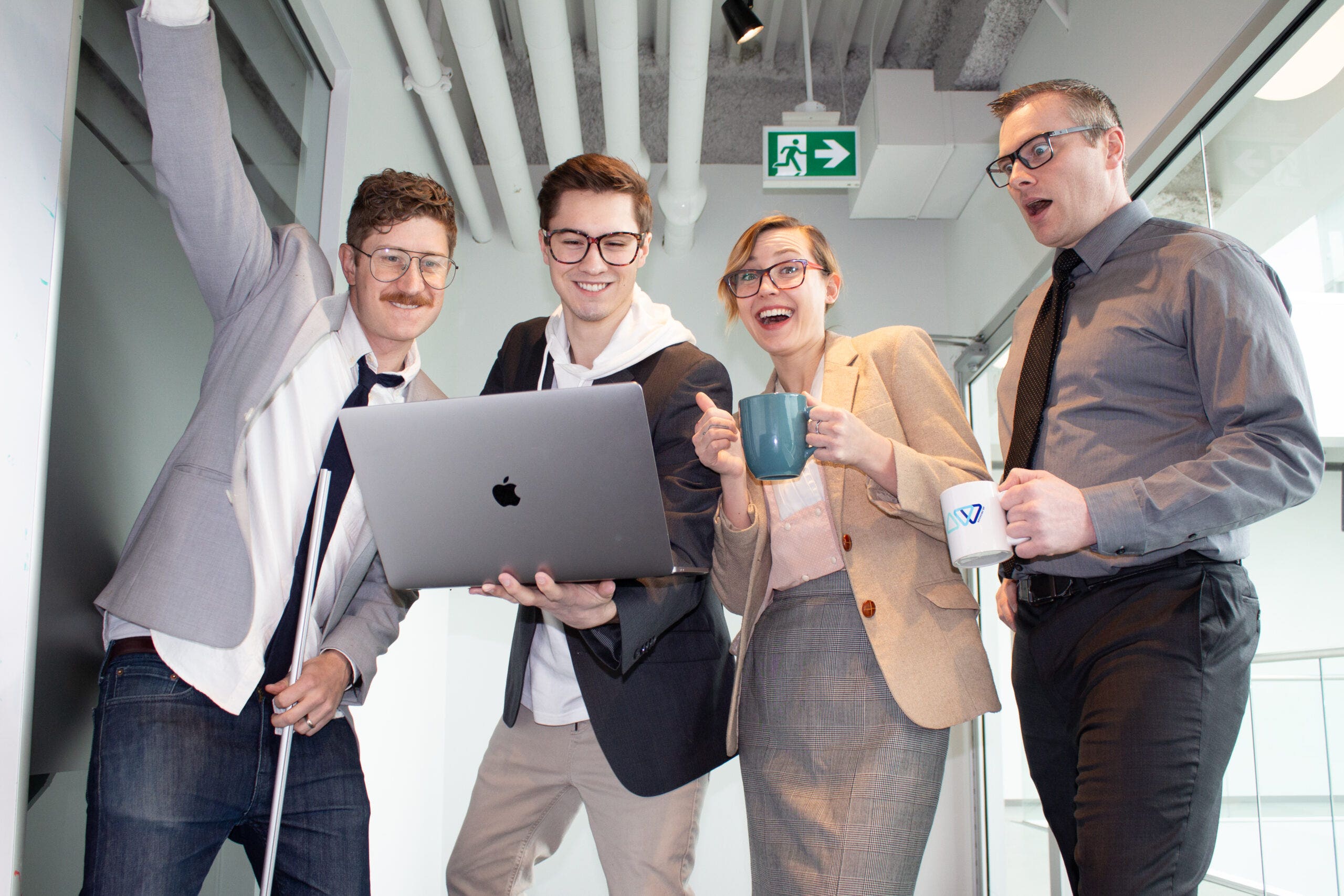 Four Twirling Umbrellas team members in office attire laugh and hold up a laptop, recreating a playful, classic stock photo moment.