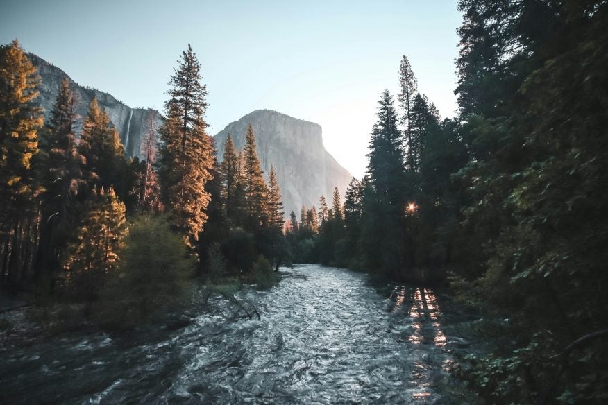 Sunset shot of landscape in Yosemite National Park with mountains in the background and trees on either side.